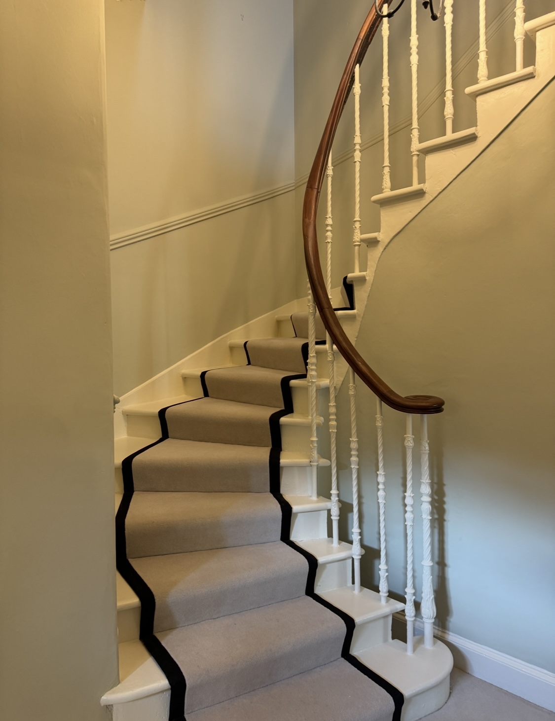 Decorated spiral stairs with a rug running down the middle with a classic wooden banister and neutral coloured walls