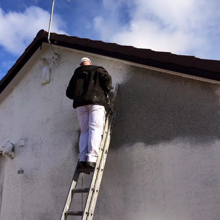 Man in overalls on a ladder painting a building